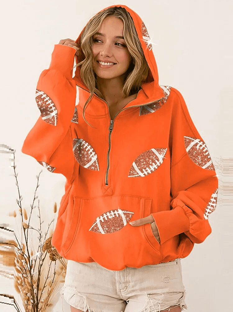 Woman wearing an orange sporty casual hoodie with front pockets, hood, and sequin football designs, styled with white shorts.